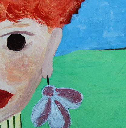 Close-up of a colorful painted portrait showing part of a face with red hair, a large black eye, and a dangling flower earring against blue sky and green ground.